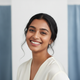 Smiling young South Asian woman, headshot portrait, against a bright white and blue background.